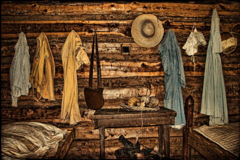 Quarto de uma casa na zona rural, com chapéu de palha pendurado na parede, algumas roupas pelo ambiente e um bolsa também pendura.